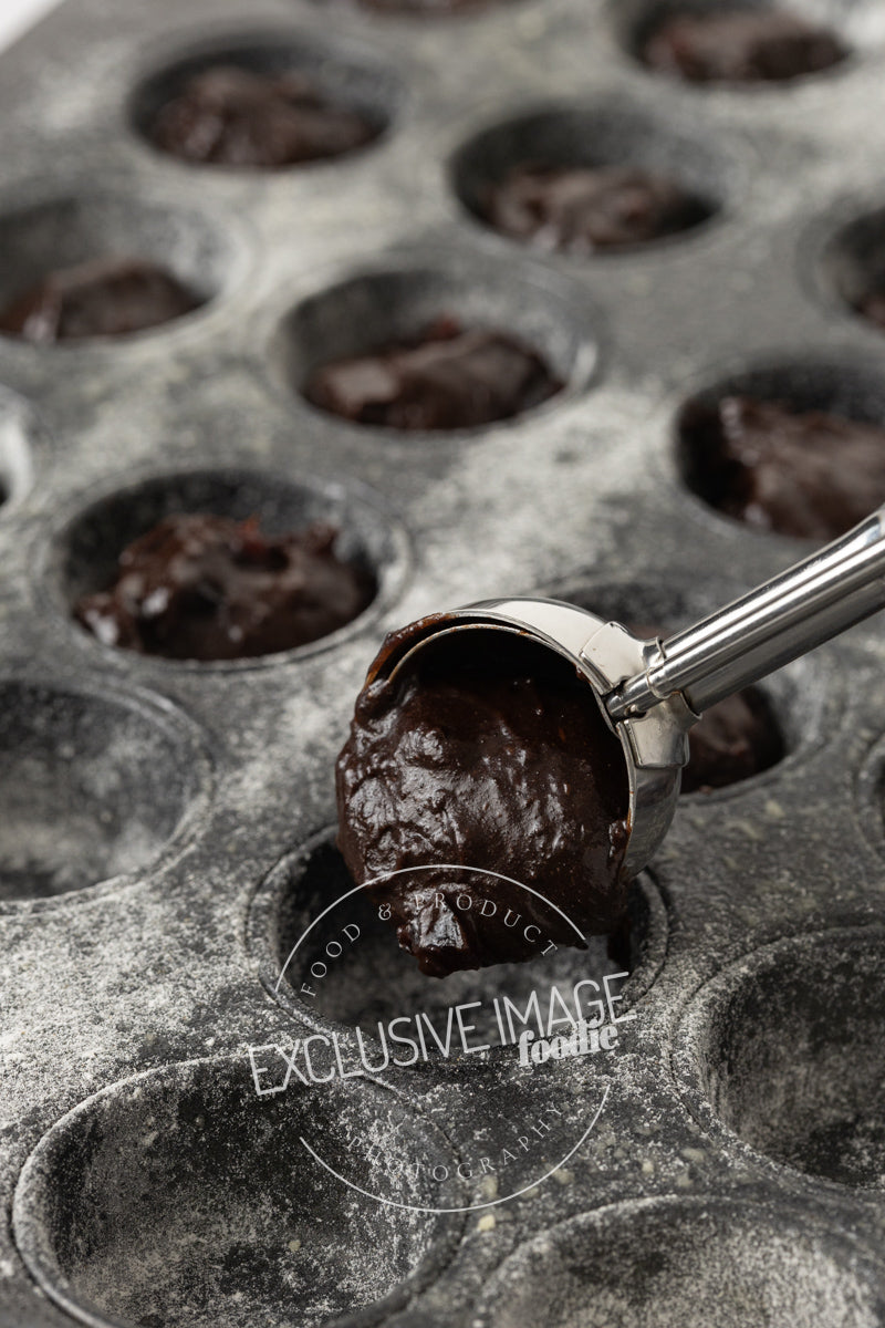 Glossy brownie batter being scooped into a mini muffin tin
