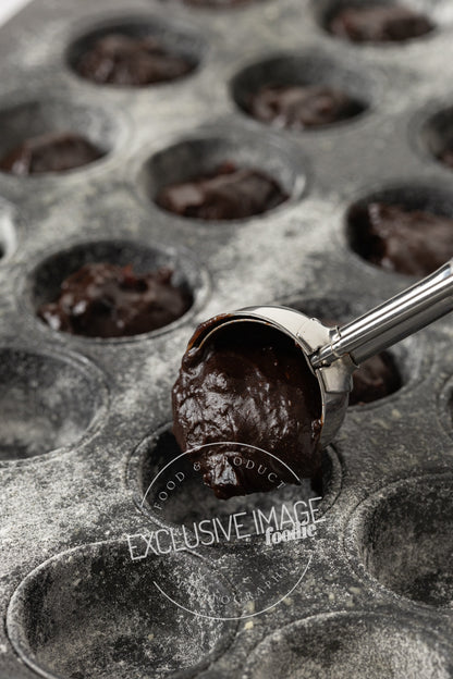 Glossy brownie batter being scooped into a mini muffin tin