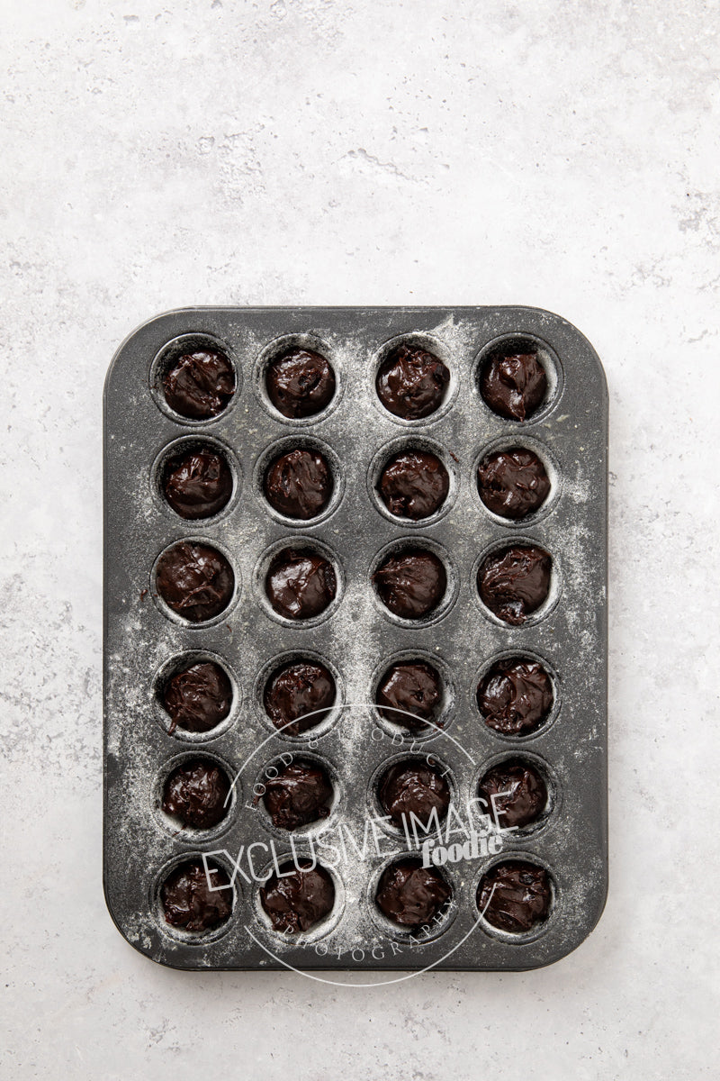 Mini muffin baking tray with brownie batter on a light gray background