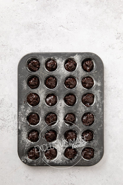 Mini muffin baking tray with brownie batter on a light gray background