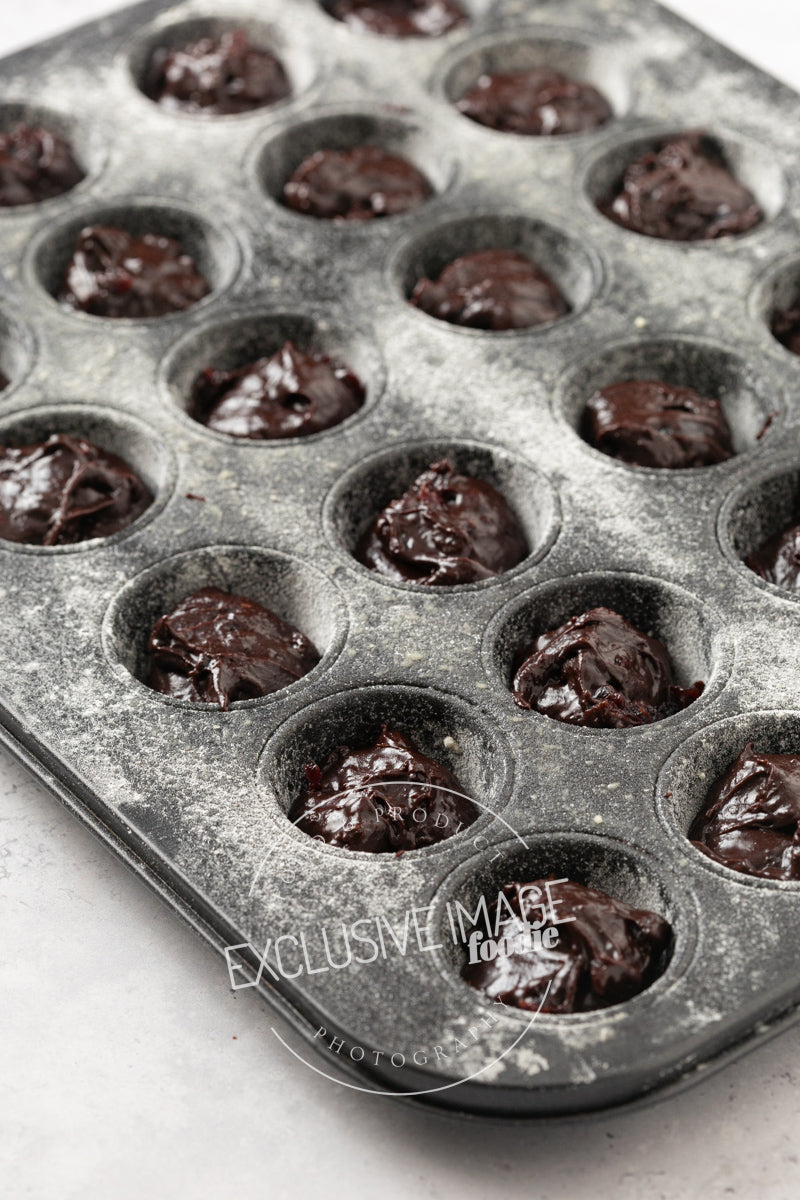 Muffin tin with brownie batter in each cup on a white background