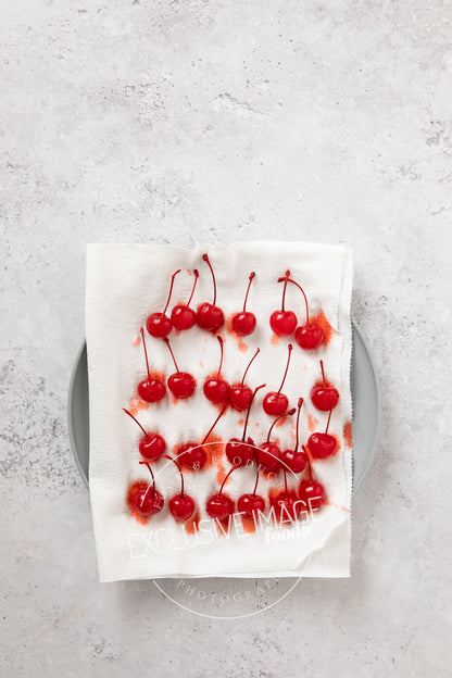 Red maraschino cherries on a white paper towel on a gray surface