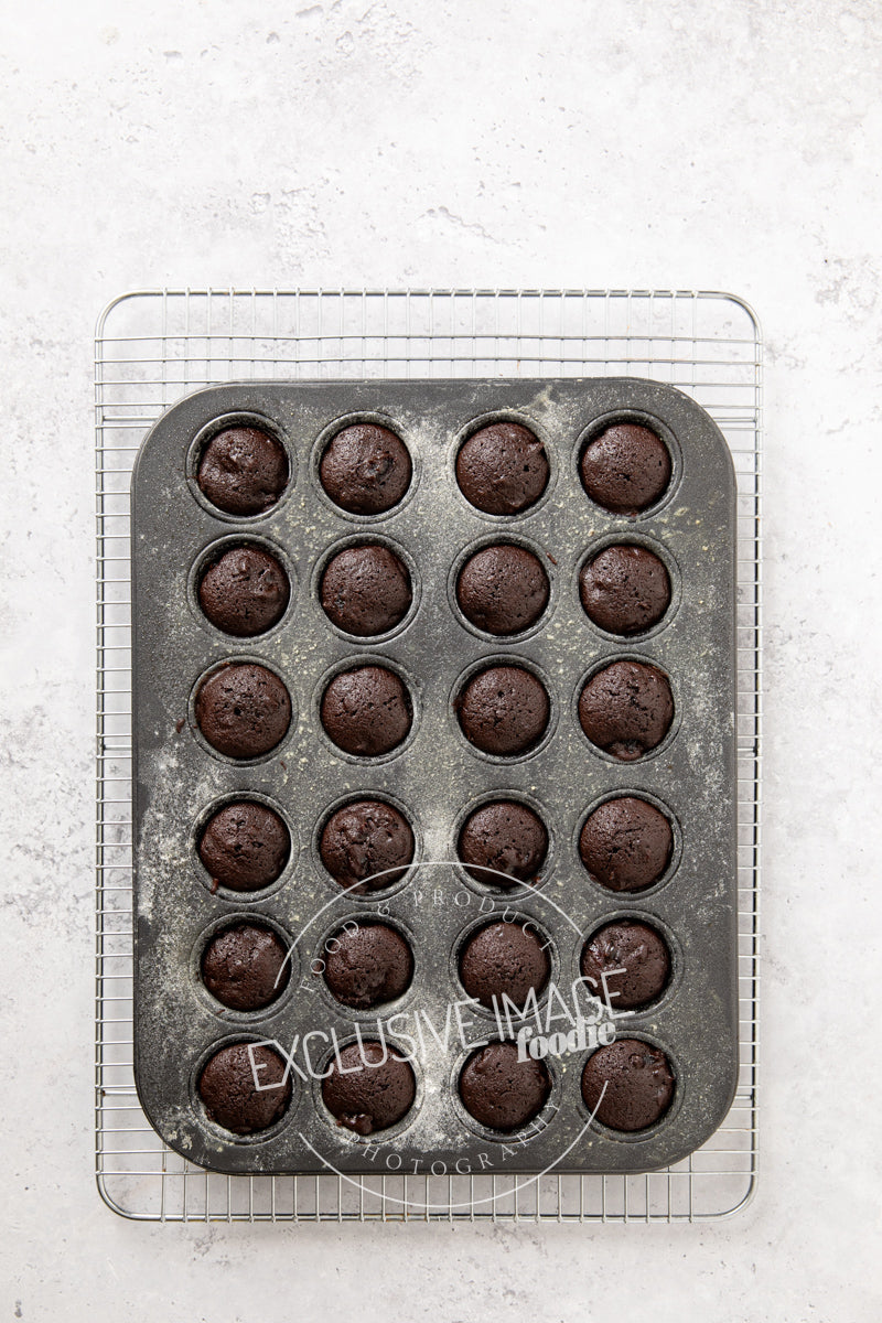 Baked mini brownies in a metal muffin tin on a light gray surface.