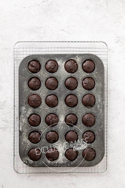 Baked mini brownies in a metal muffin tin on a light gray surface.