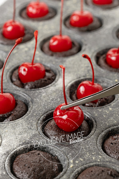 Tweezers placing a maraschino cherry on a baked brownie in a mini muffin pan