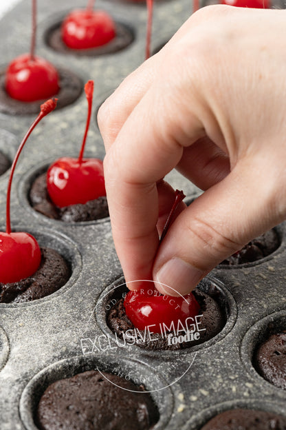 Hand placing a cherry on top of a brownie in a mini muffin tin.