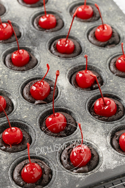 Chocolate brownie mini muffin cups with red cherries on a gray surface