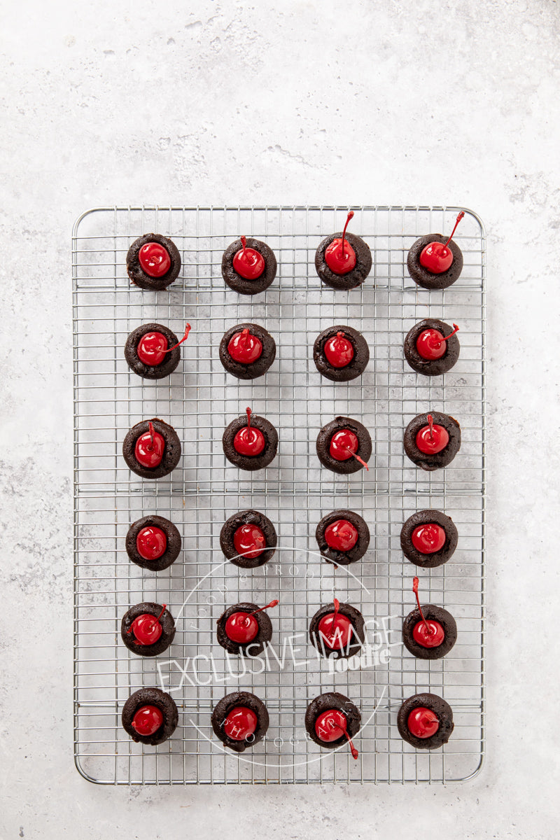 Chocolate mini brownies with red cherries on a cooling rack against a light gray background