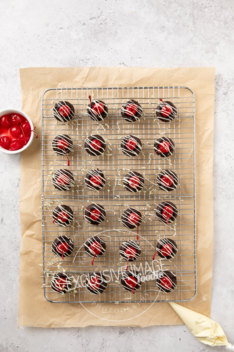 Wire cooling rack with chocolate-brownie bites with cherries on a light gray surface