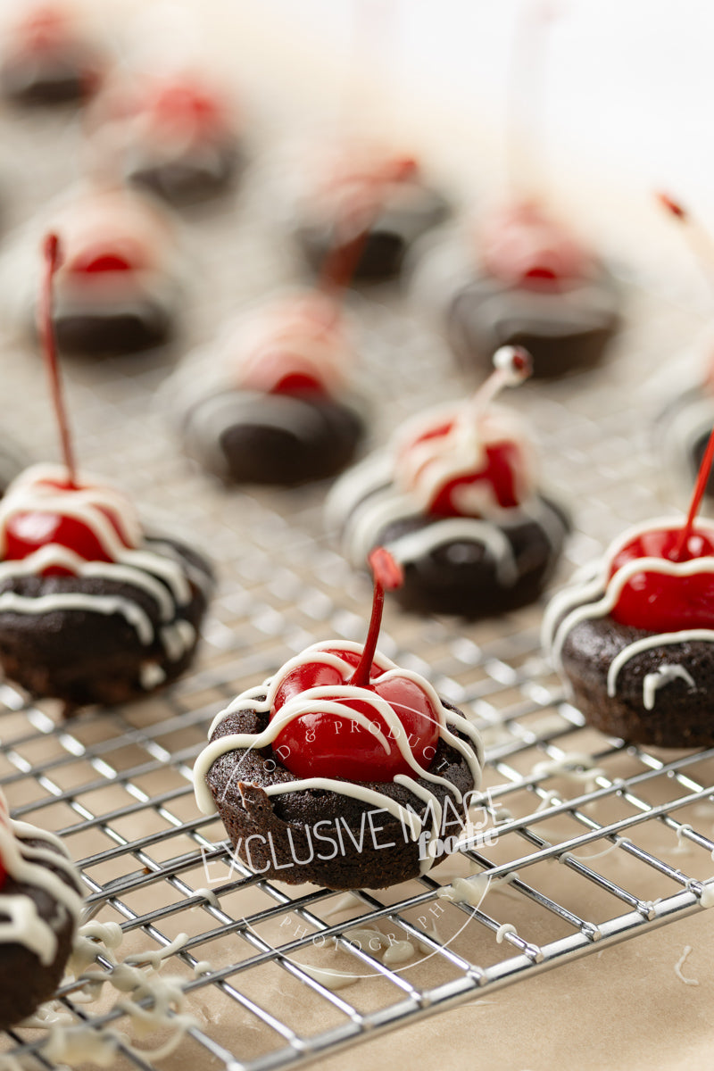 Chocolate mini brownies with cherries on a cooling rack over brown parchment paper.