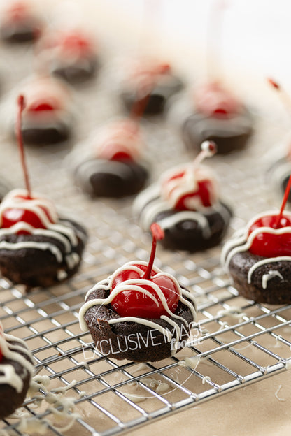 Chocolate mini brownies with cherries on a cooling rack over brown parchment paper.