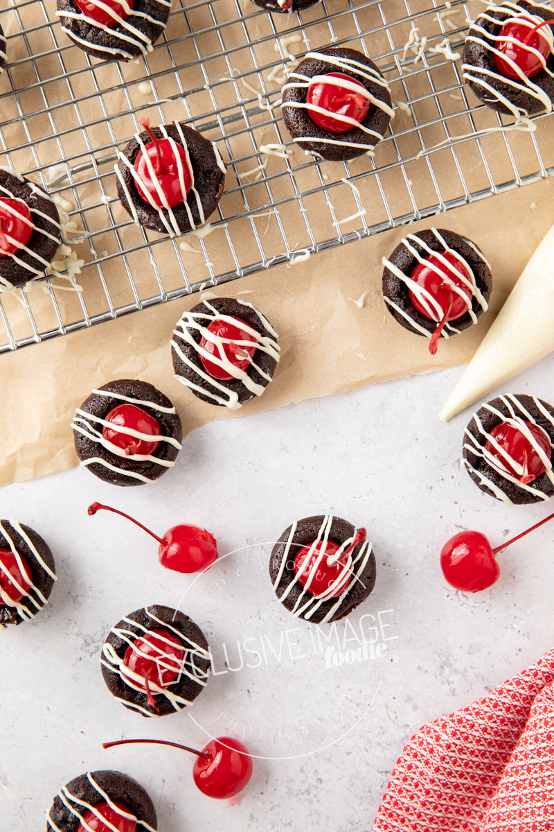 Chocolate brownie bites with cherry toppings on a cooling rack and surface.