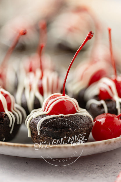 Chocolate mini brownies with a cherry on top on a plate, blurred background