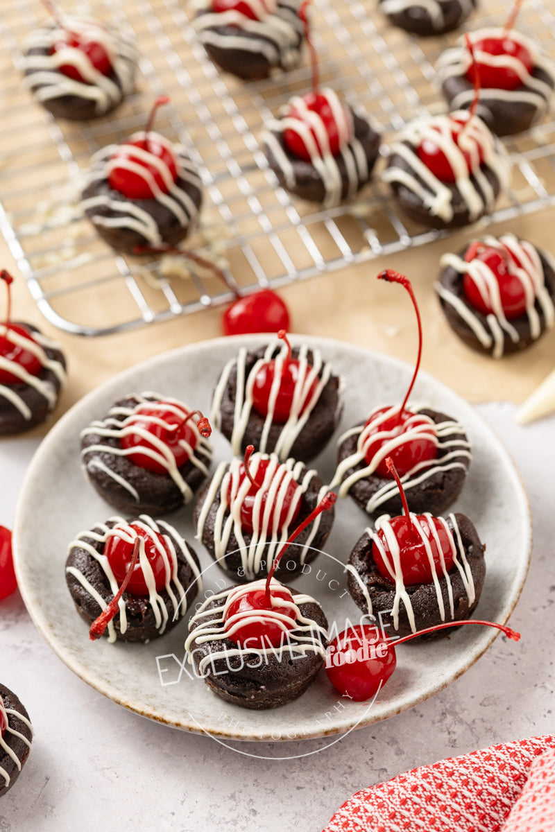 Chocolate mini brownies with cherries on a plate and cooling rack.