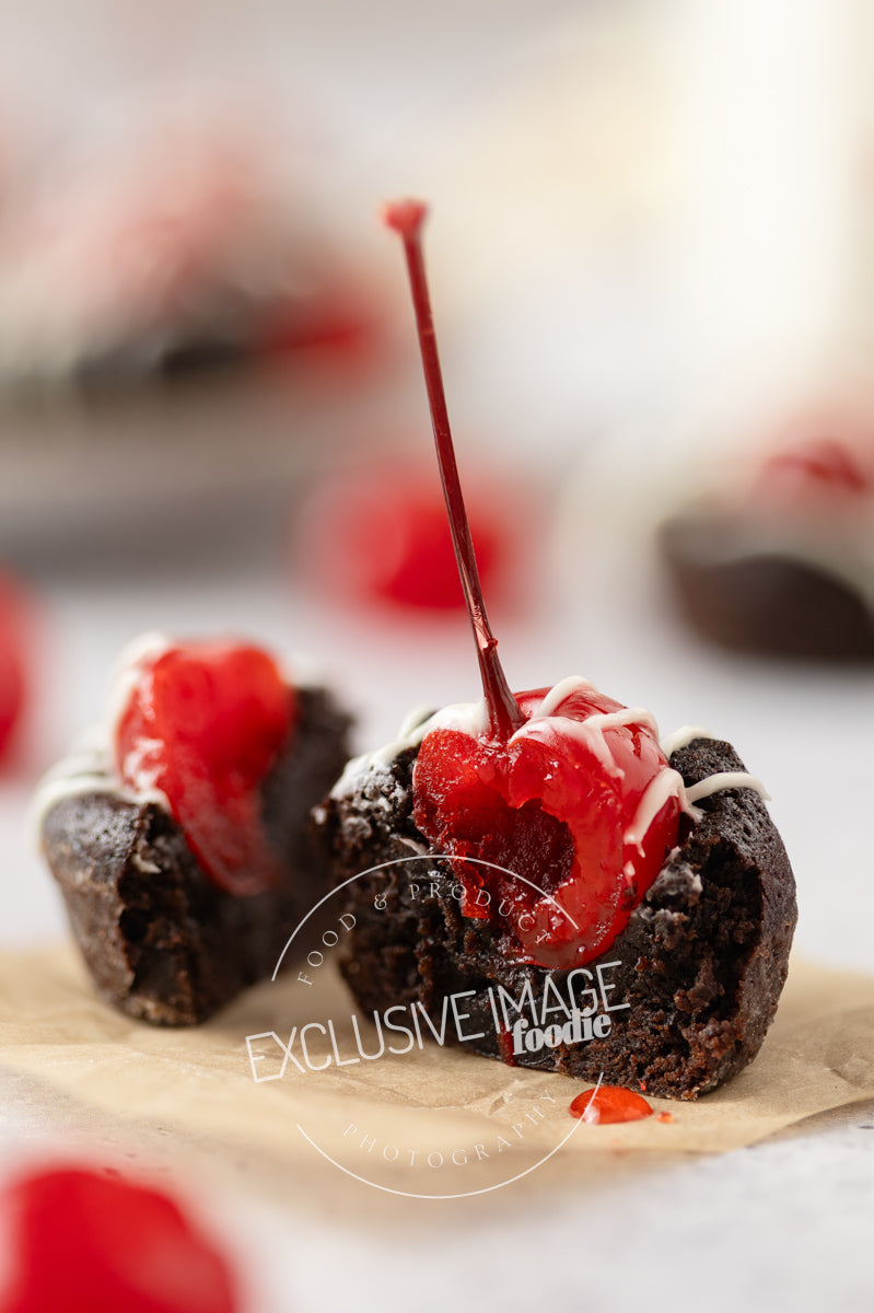 Cut-open chocolate 2 bite brownies with a cherry on top on a white background