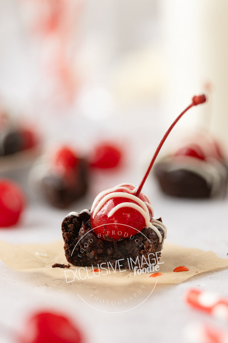 Cut-open 2 bite brownie with cherry on top on a white background