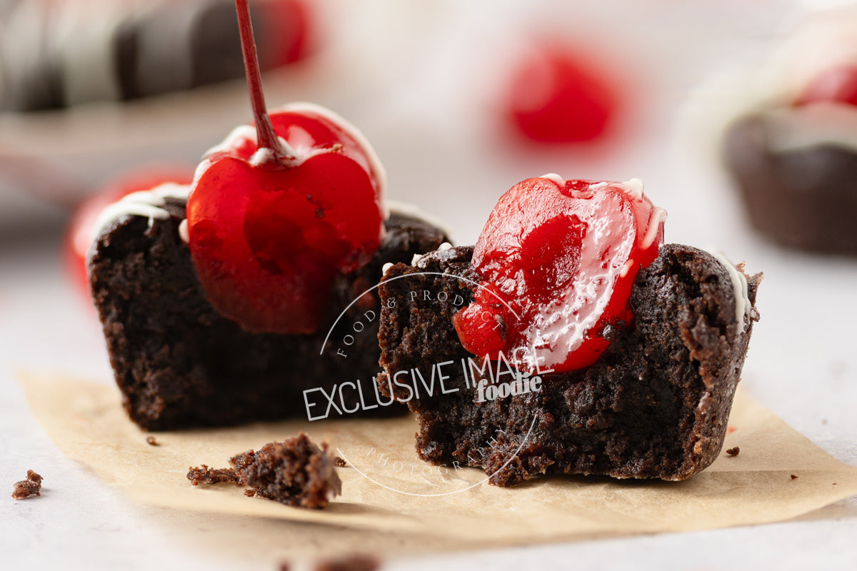 Chocolate mini brownie with cherry on top on parchment paper and a blurred background