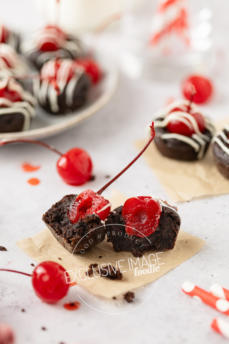 Cut-open 2 bite brownie with cherries on a white surface