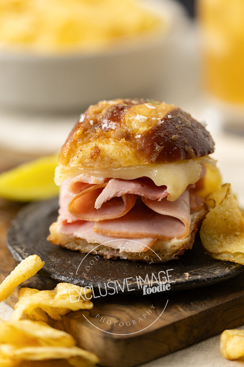 Ham and cheese slider on a black plate with chips and a blurred background