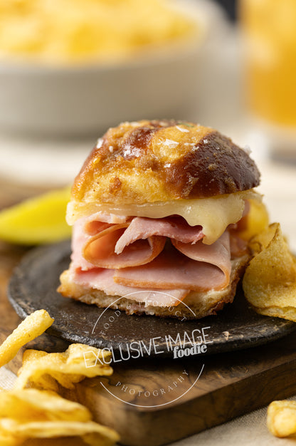 Ham and cheese slider on a black plate with chips and a blurred background