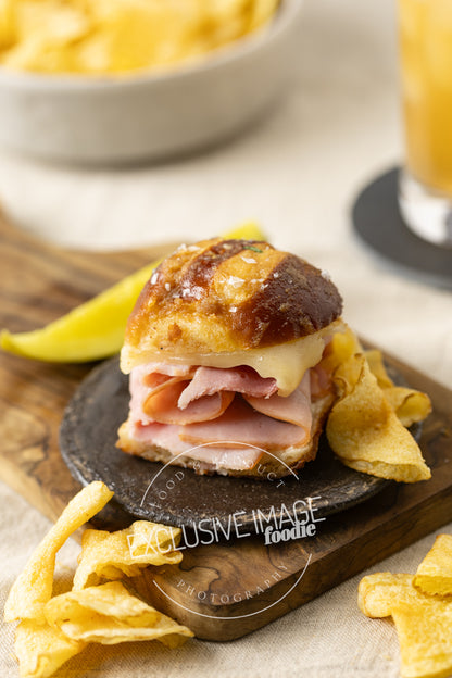 Ham and cheese slider on a bun with chips and a drink in the background