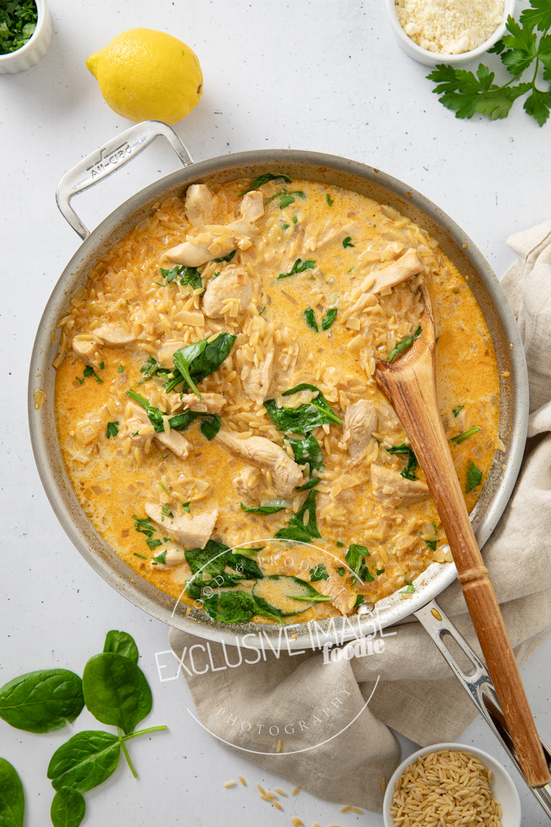 Creamy chicken and spinach dish in a pan with a wooden spoon, surrounded by herbs and a lemon.