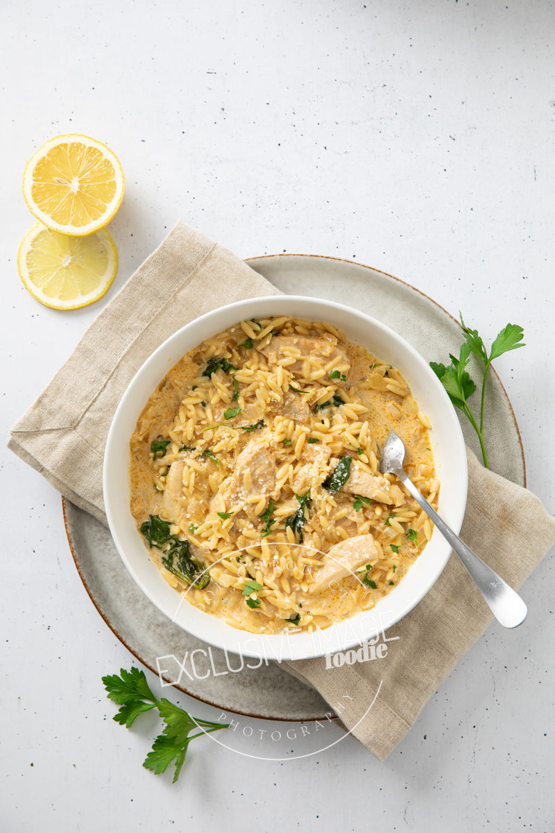 Bowl of creamy chicken and rice dish with lemon wedges on a light background