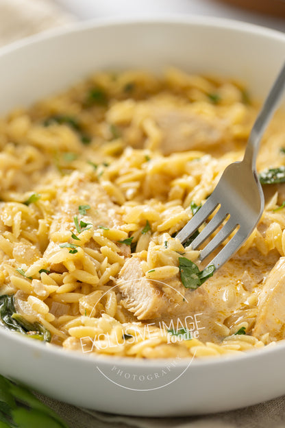 Close-up of a bowl of creamy pasta with chicken and spinach, featuring a fork.