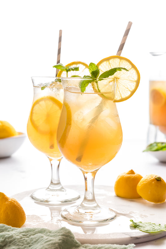 Two glasses of orange lemonade with lemons and mint leaves on a white background