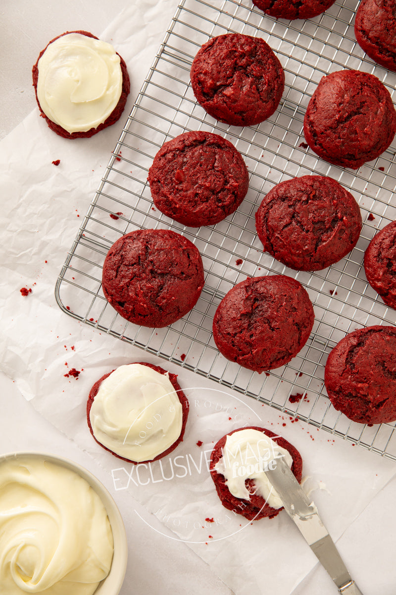 Red velvet cookies with cream cheese frosting on a cooling rack.