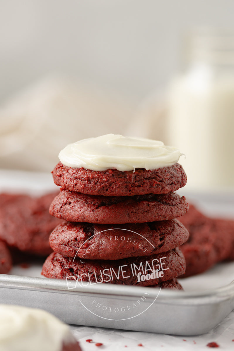 Stack of red velvet cookies with white frosting on a marble surface.