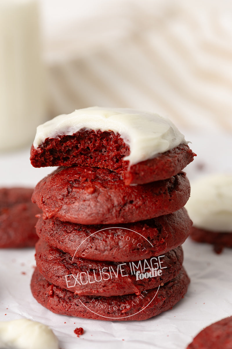 Stack of red velvet cookies with cream cheese frosting on a white background