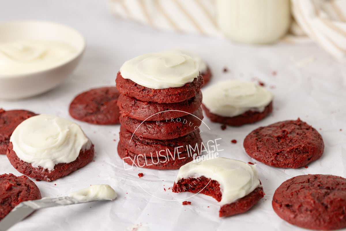 Red velvet cookies with cream cheese frosting on a light surface.